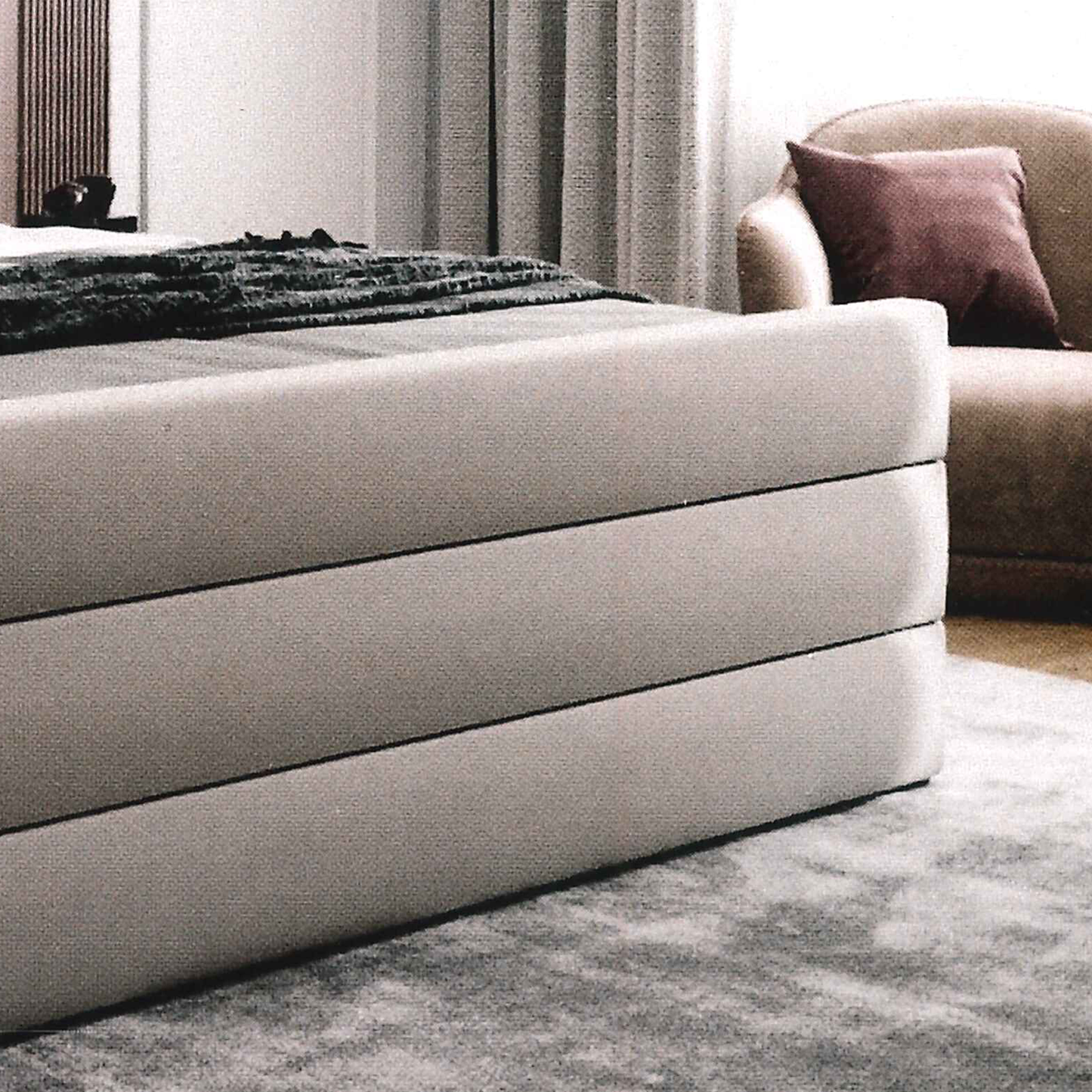 Gray bespoke upholstered bed with horizontal lines in a room with a sofa and curtains