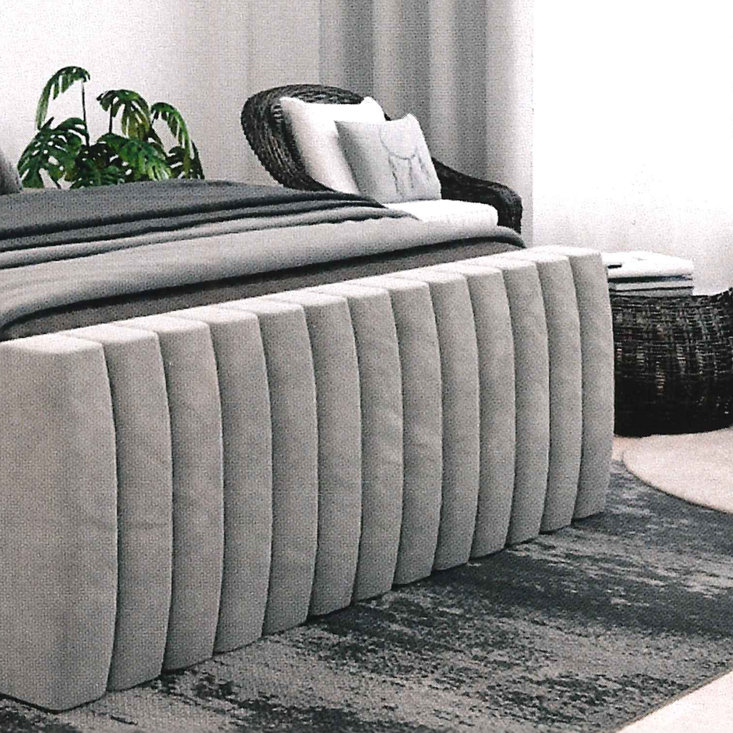 Gray upholstered footborard, vertical lines in a room with a plant and wicker chair.