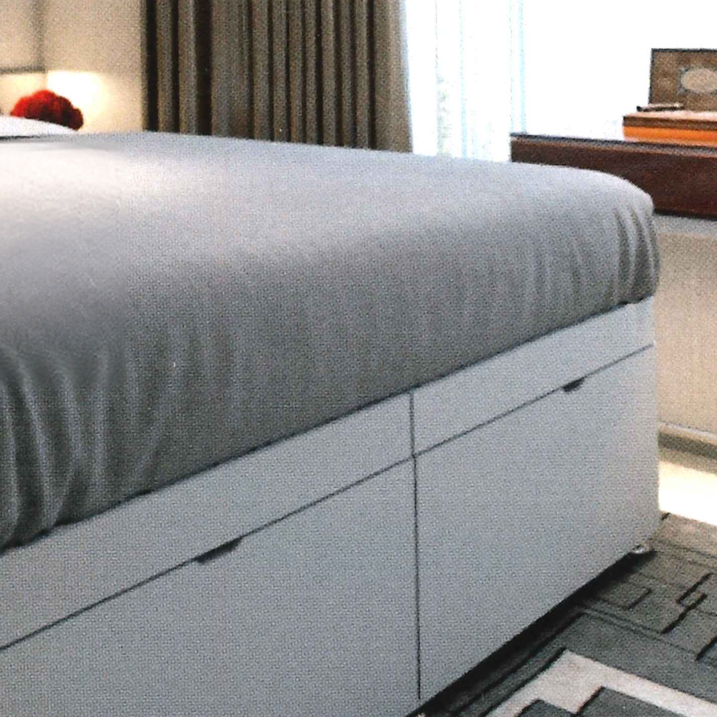 Gray upholstered bed with Ottoman storage in a bedroom setting.