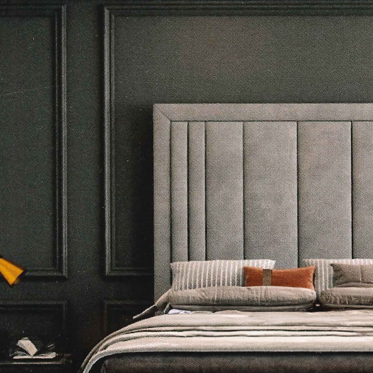 Gray upholstered bespoke headboard with pillows against a dark paneled wall