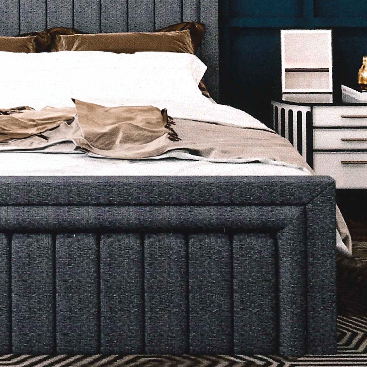 Gray upholstered bed, matching footboard with white bedding and brown pillows in a bedroom setting.