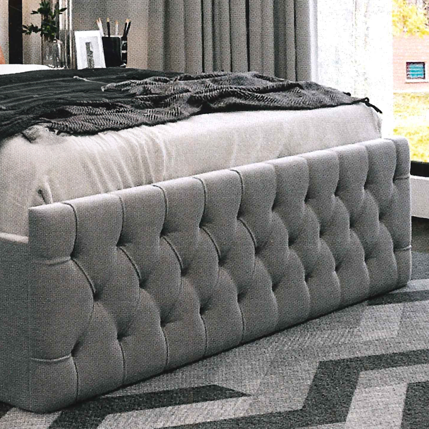 Gray tufted bed with a scroll-style textured headboard in a room setting.