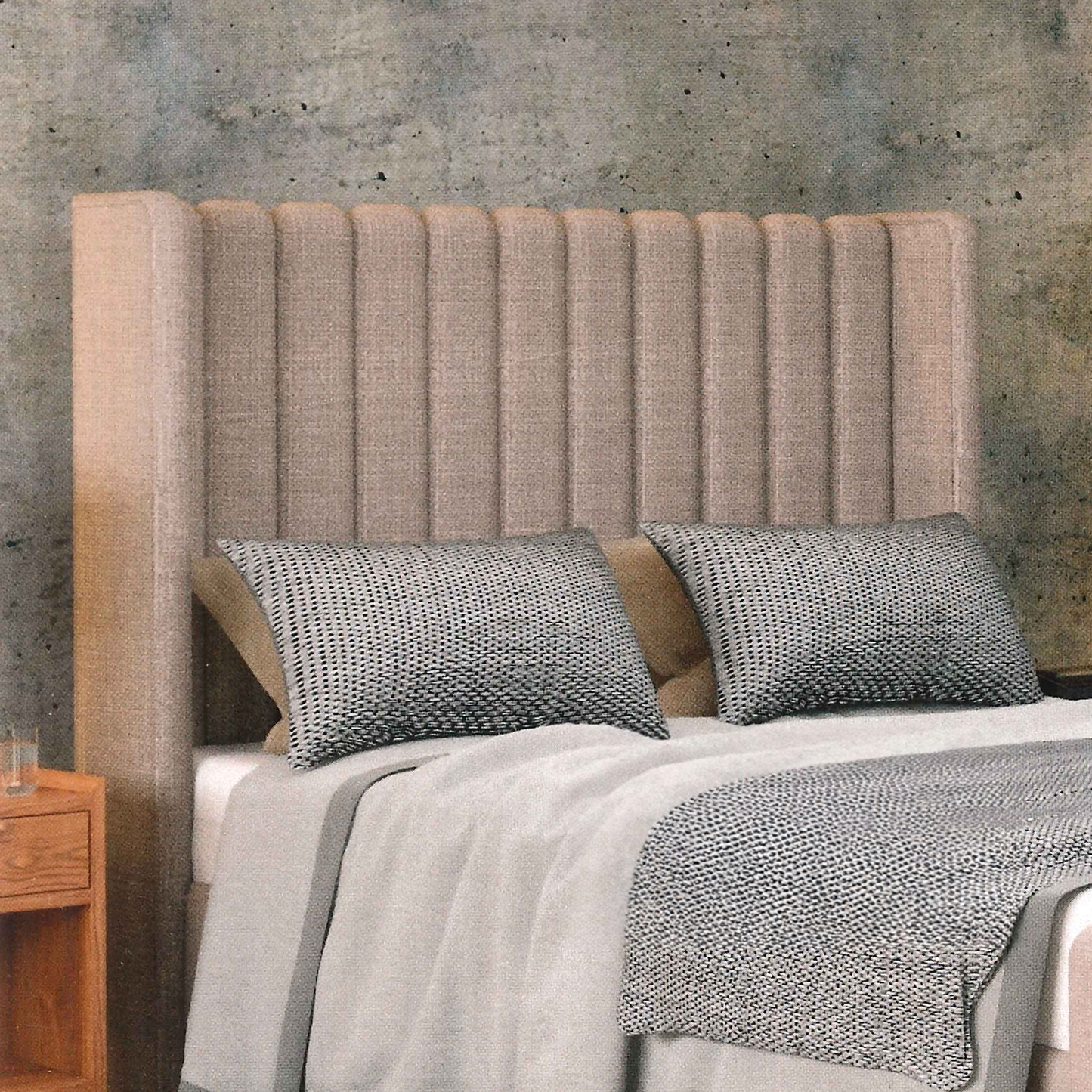 Bed with textured headboard and gray bedding against a concrete wall.