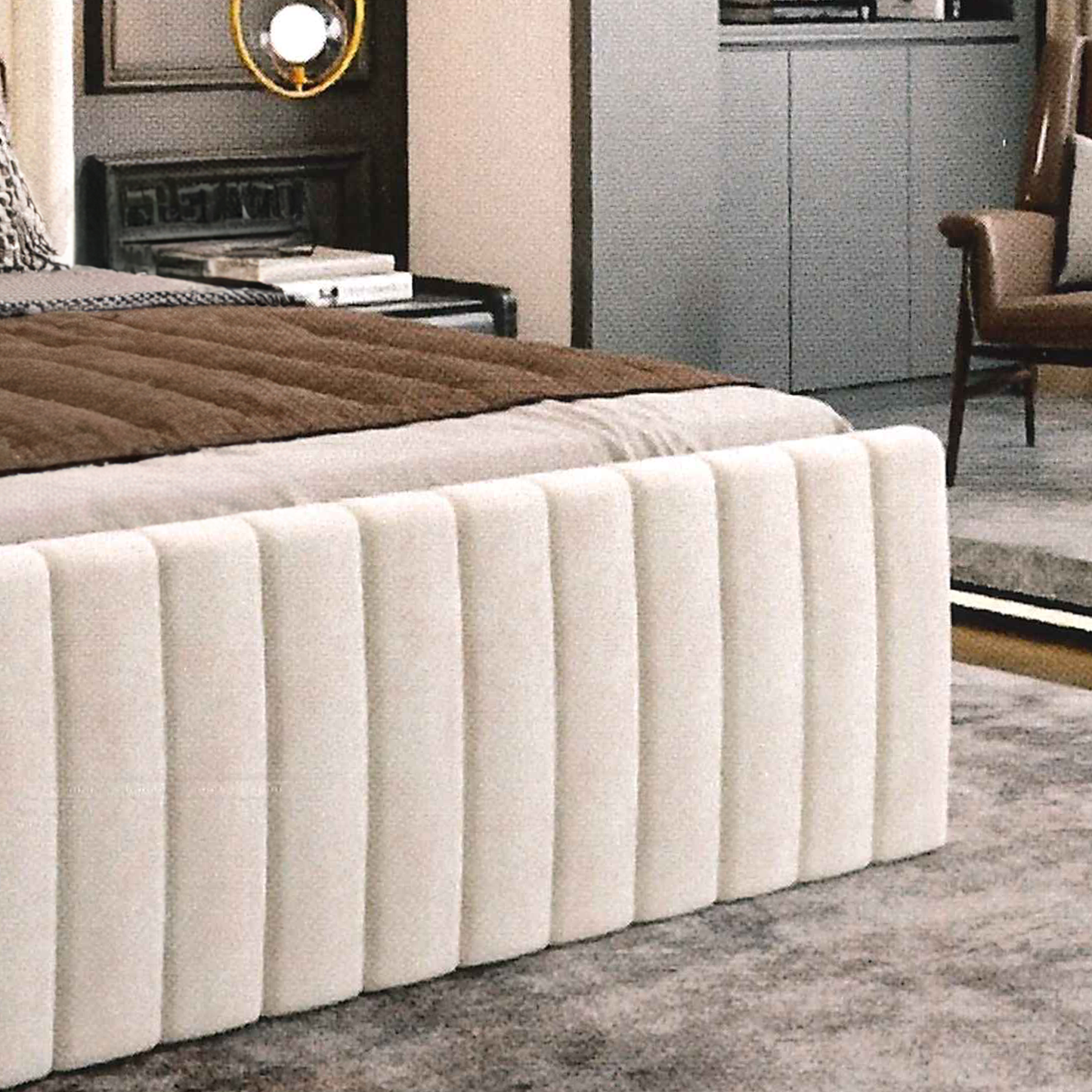Beige upholstered bed in a room with a chair and fireplace.
