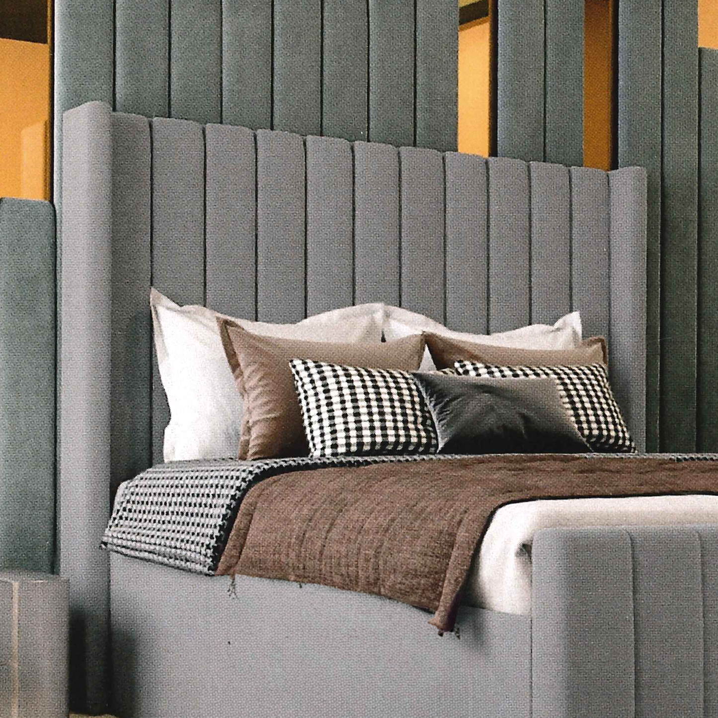 Gray upholstered bed with decorative pillows and a checkered blanket against a gray wall.