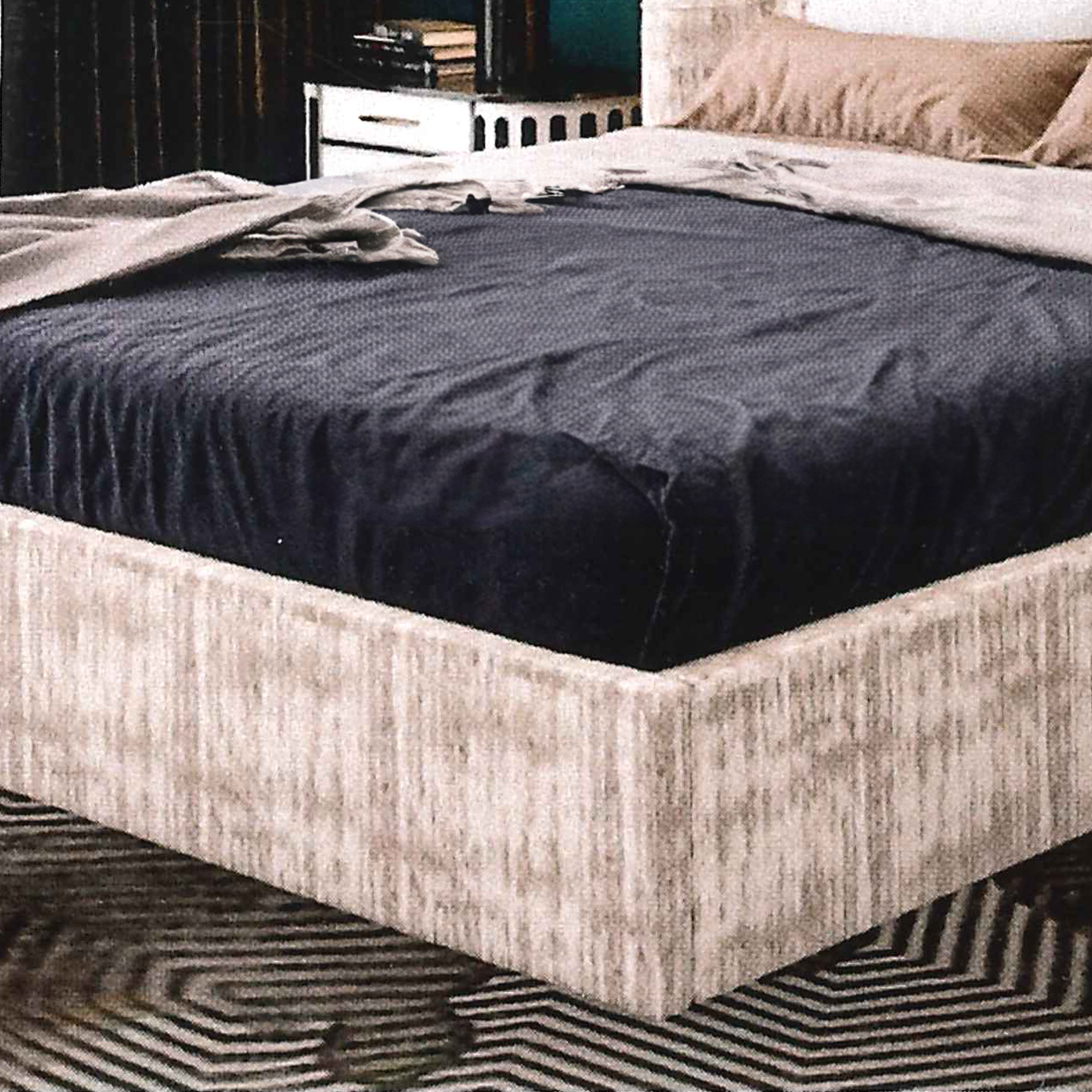 Bed with dark blue mattress cover and beige bed frame in a bedroom setting.