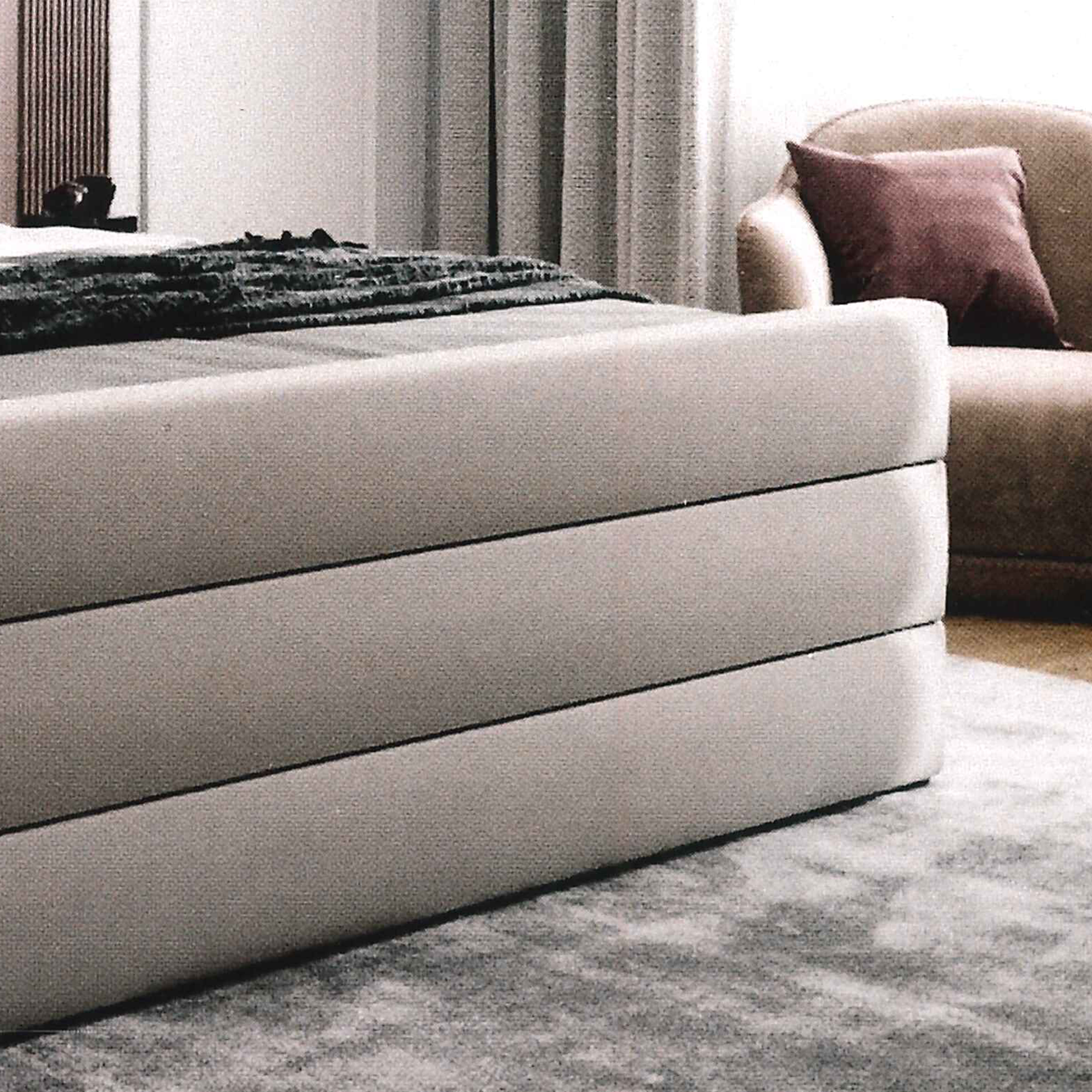 Gray bespoke upholstered bed with horizontal lines in a room with a sofa and curtains
