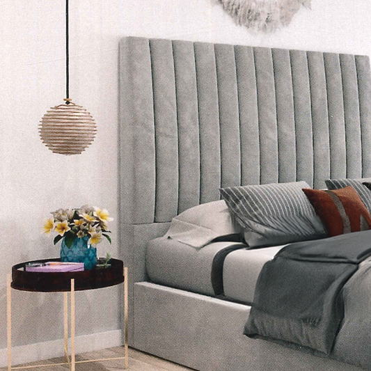 Gray upholstered bed, vertical lines headboard with decorative pillows and a side table with flowers in a bedroom setting.