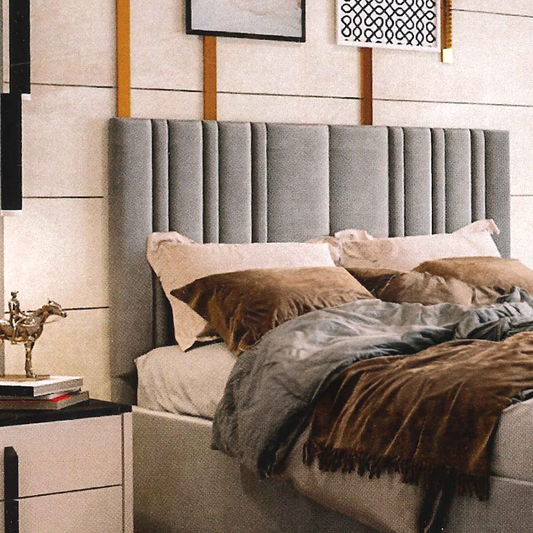 Gray upholstered headboard with pillows and blankets in a bedroom setting.
