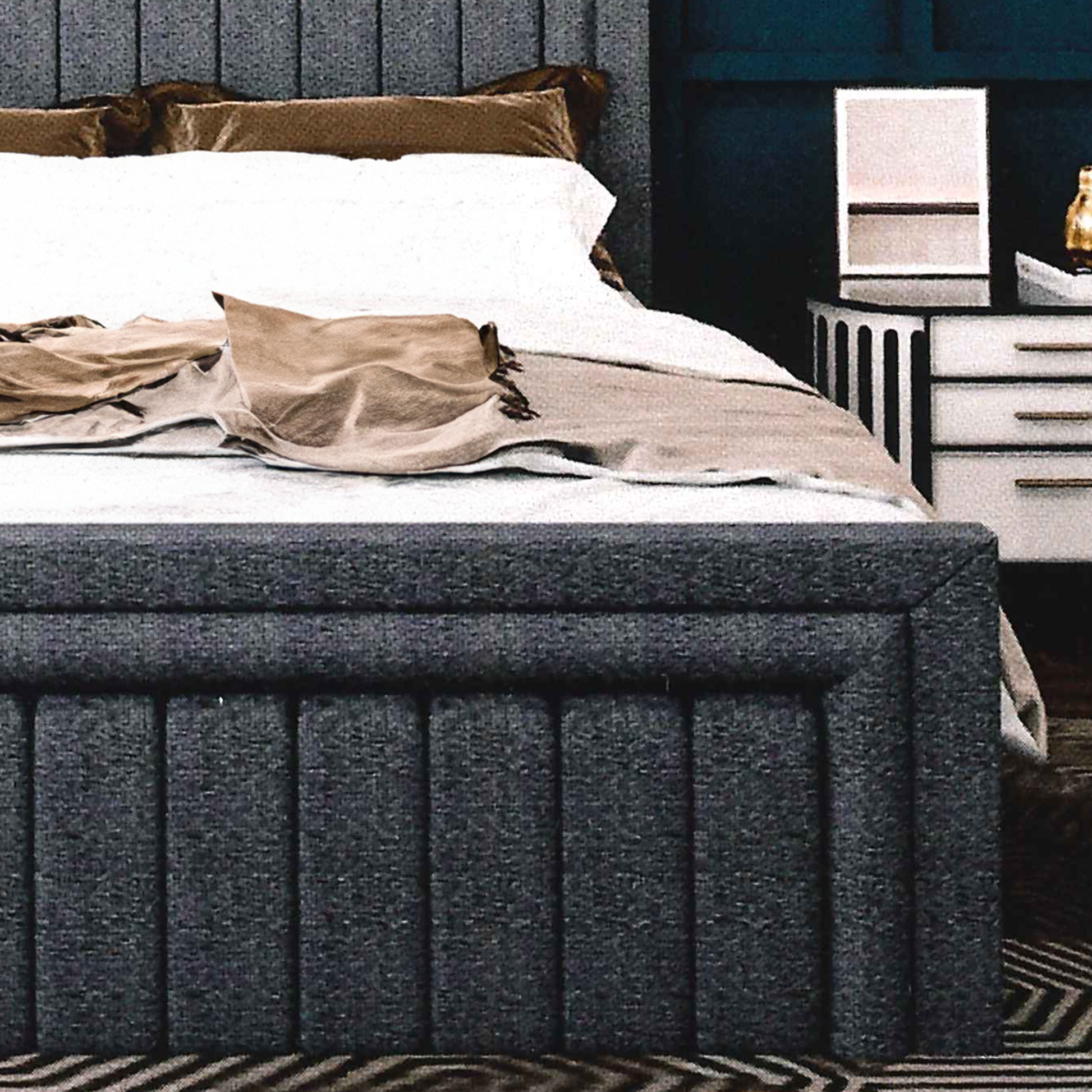 Gray upholstered bed, matching footboard with white bedding and brown pillows in a bedroom setting.