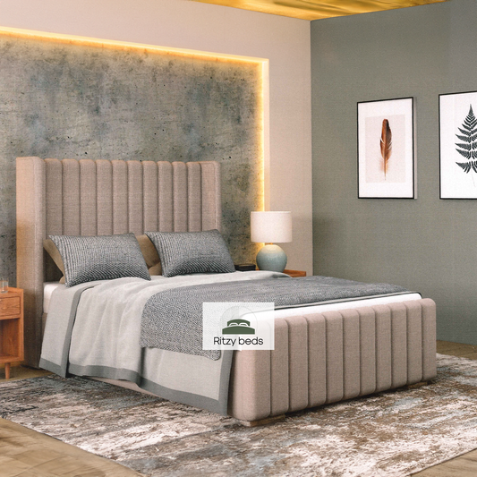 Beige winged upholstered bed with gray bedding in a modern bedroom setting, featuring the Ritzy Beds logo.