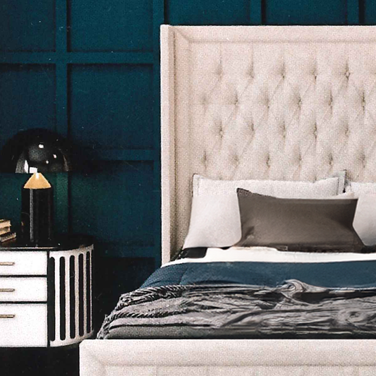 Beige upholstered bed with dark blue bedding against a teal wall.