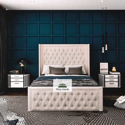 Beige tufted bed with matching headboard against a dark blue paneled wall, featuring 'Ritzy Beds' logo.