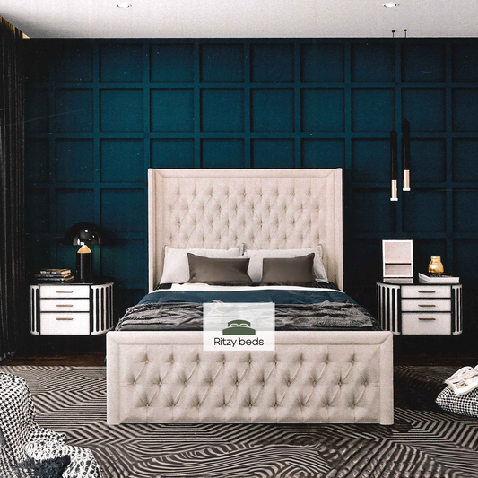 Beige tufted bed with matching headboard against a dark blue paneled wall, featuring 'Ritzy Beds' logo.