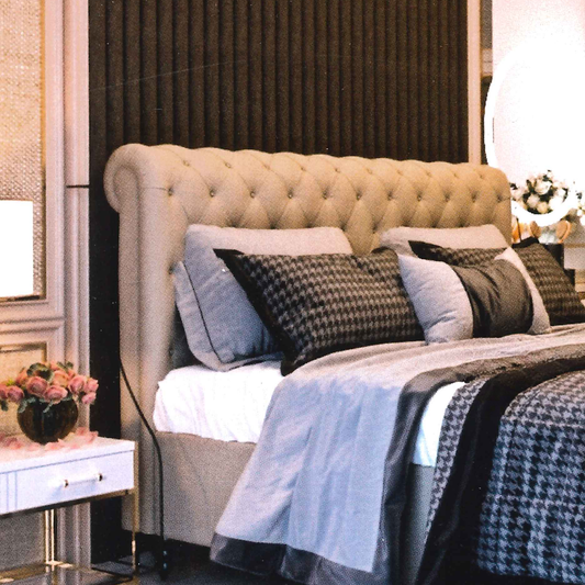 Neatly made luxury bed with decorative pillows and a tufted scroll headboard in a bedroom setting.