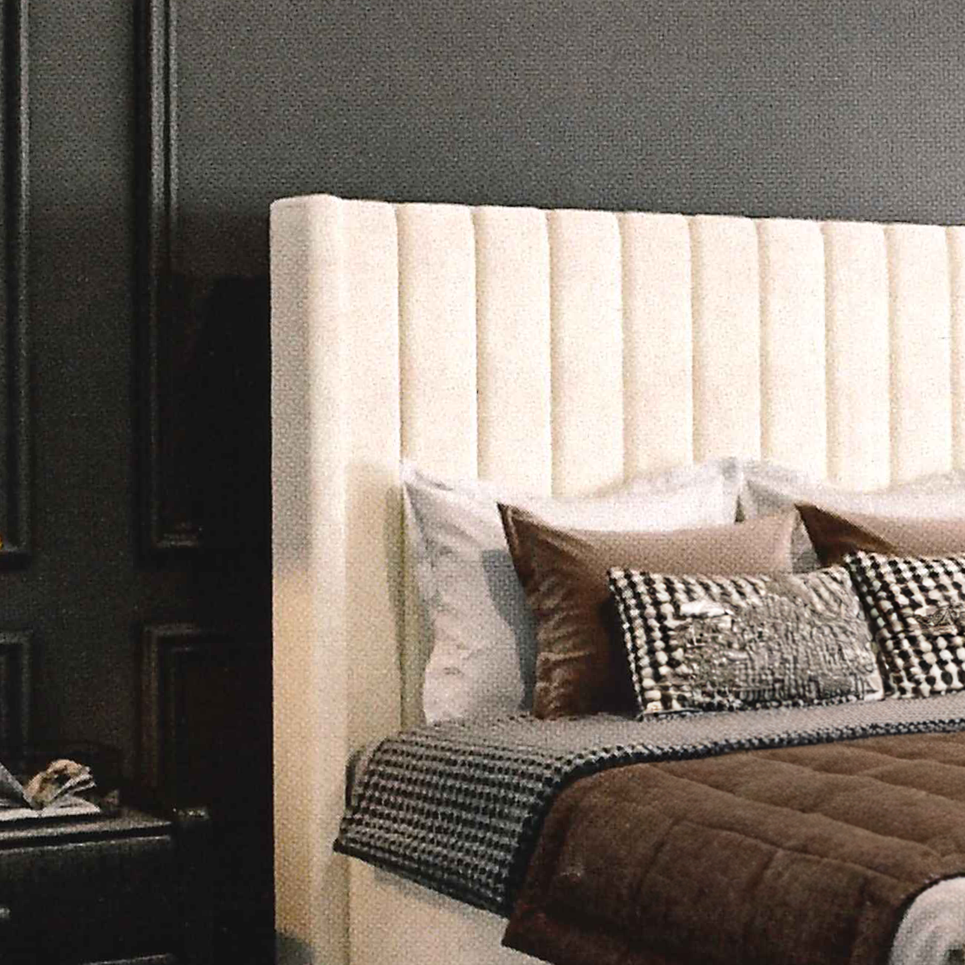 Beige upholstered headboard with decorative pillows and blankets in a bedroom setting.