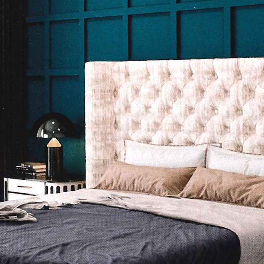Bedroom with a tufted headboard and decorative pillows against a teal wall.
